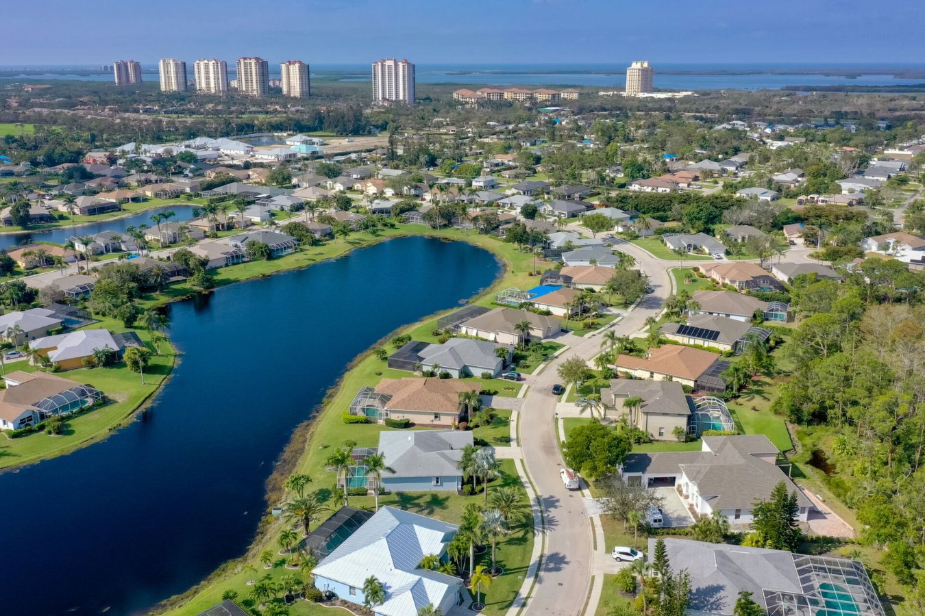 Aerial view of lakefront homes in Estero, Florida, with the bay and Gulf-front towers beyond